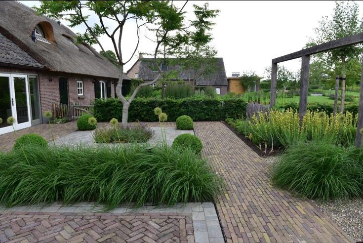 Aangelegde tuin met siergrassen, taxusbollen, sierbestrating en pergola