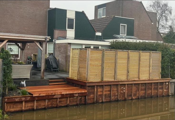 Aangelegde houten vlonder met privacyscherm bij het water